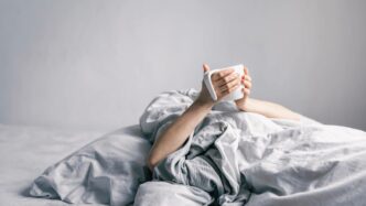 Persona sostiene taza mientras está en la cama