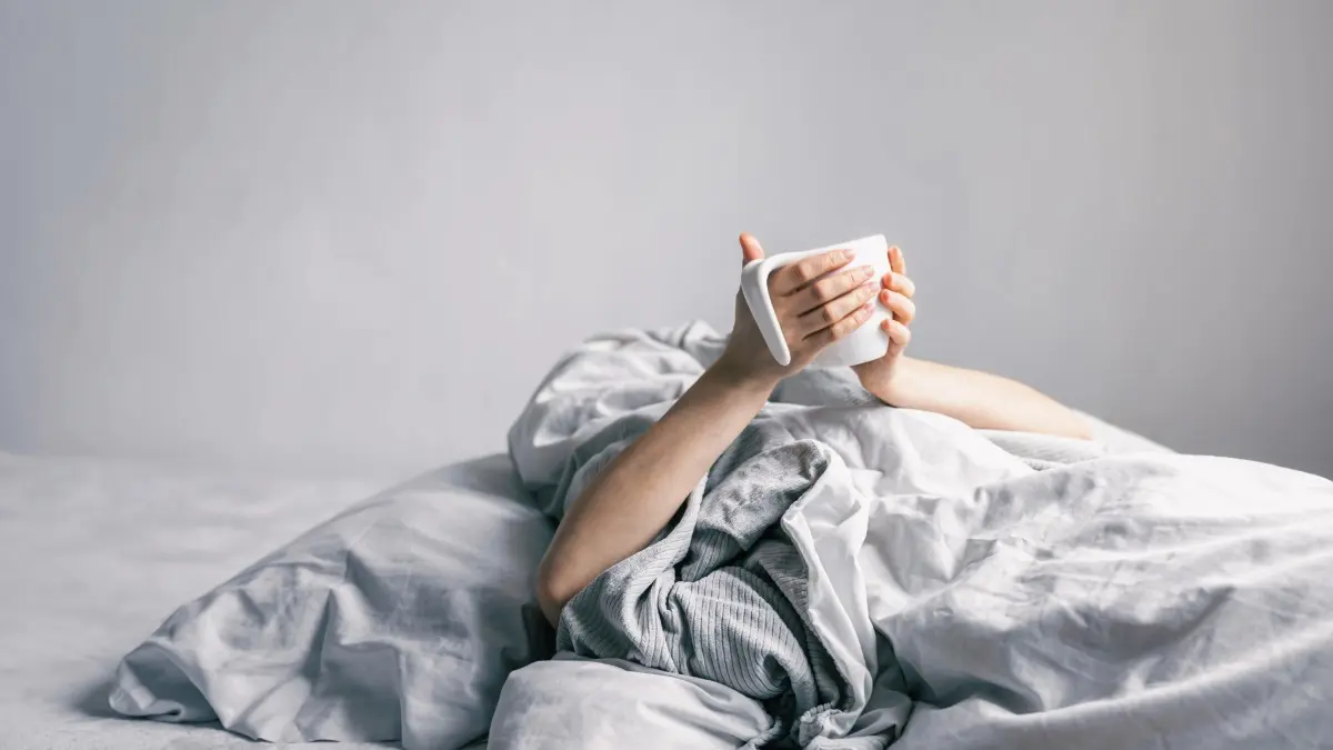 Persona sostiene taza mientras está en la cama